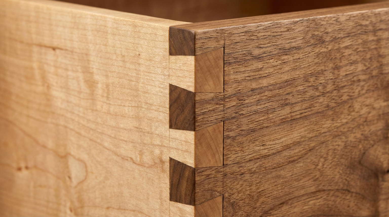 Close-up detail of hand-cut dovetail joinery on a luxury hardwood chest of drawers, showing the precise interlocking of pin and tail with hairline gaps and a smooth hand-planed surface finish in warm studio light