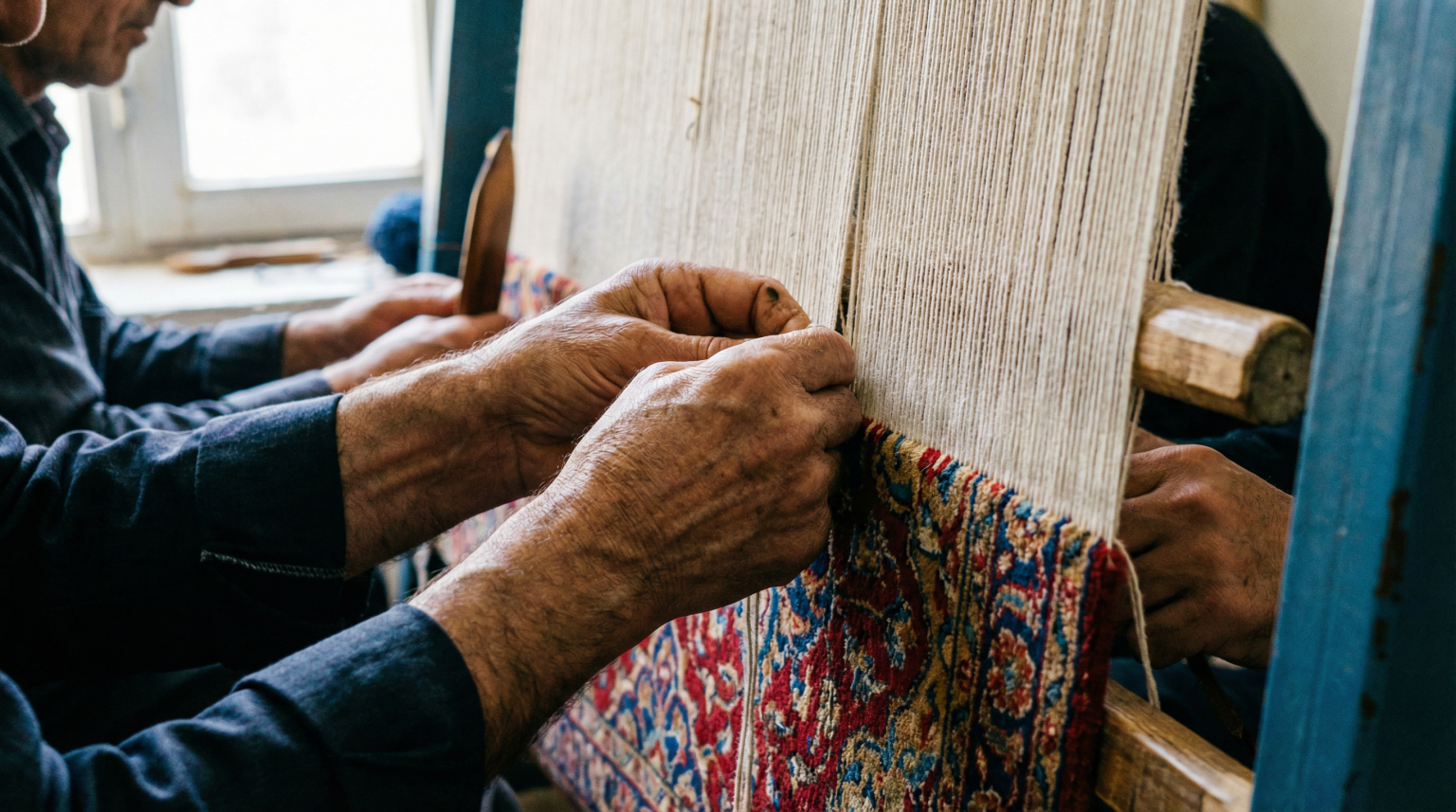 Close-up of artisans hand-knotting a Persian rug on a traditional loom