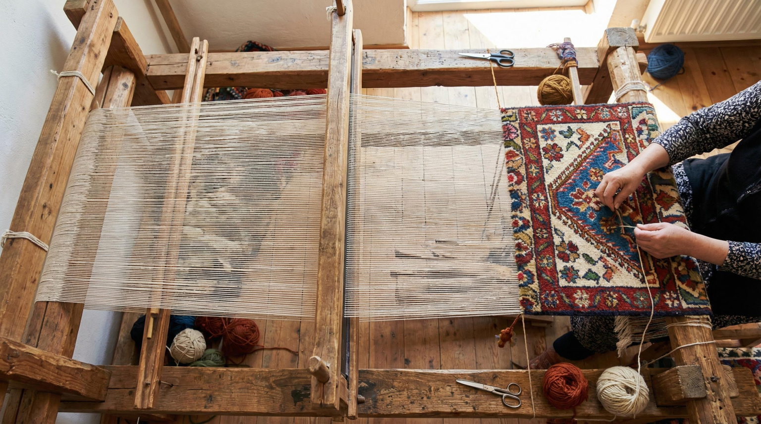 Close-up overhead view of a hand-knotted rug in progress on a loom, showing the knotting technique and dense pile structure